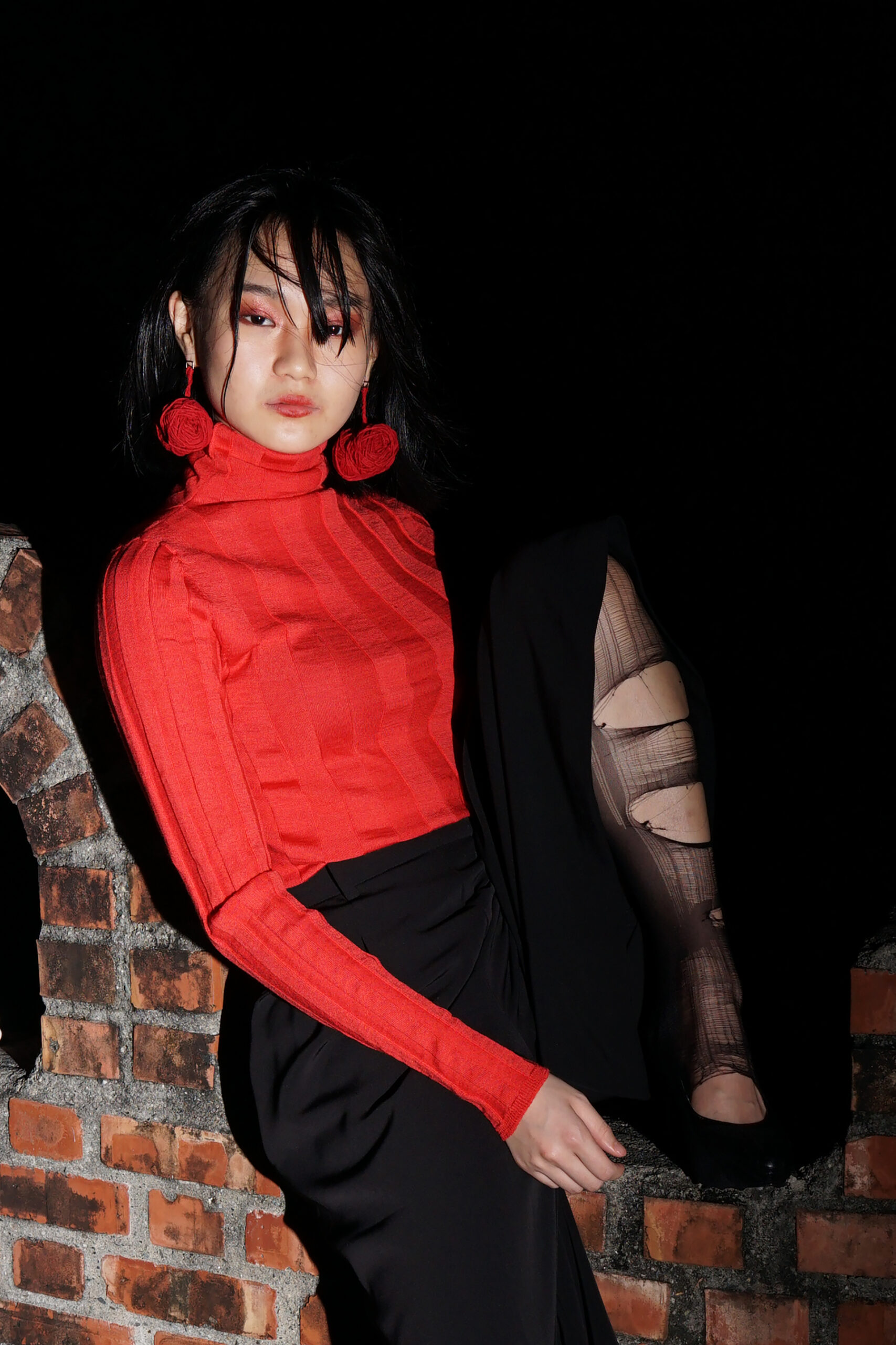 Portrait of girl sitting on a brick ledge with classic trousers and torn nylons, red turtle neck and bundle of yarn earings