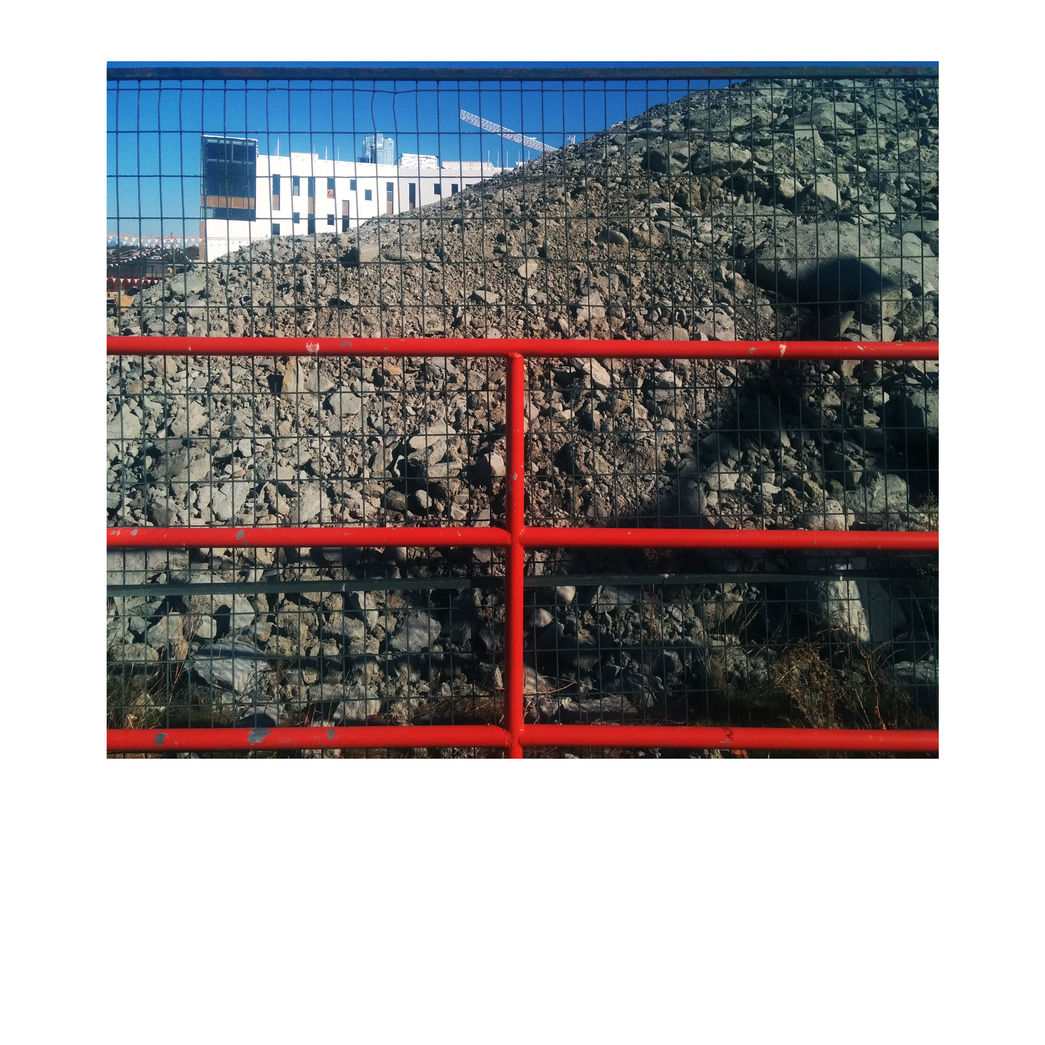 looking from behind a red metal piped fence and black mesh, to a large pile of soil, rock and rubble