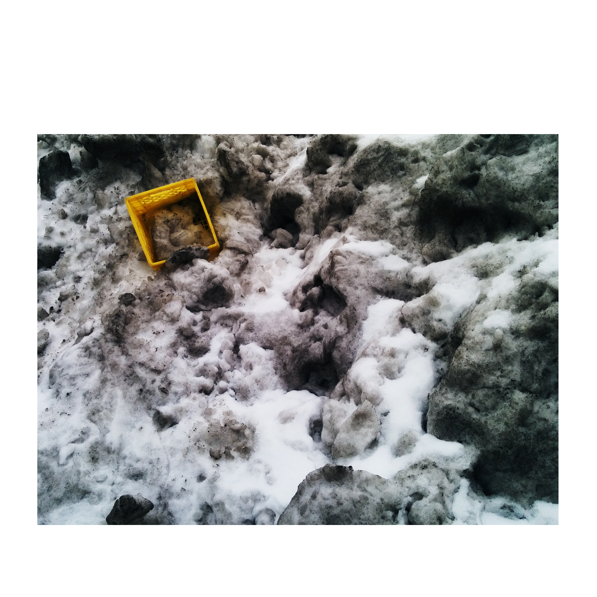 a yellow milk crate in dark dirty snow bank