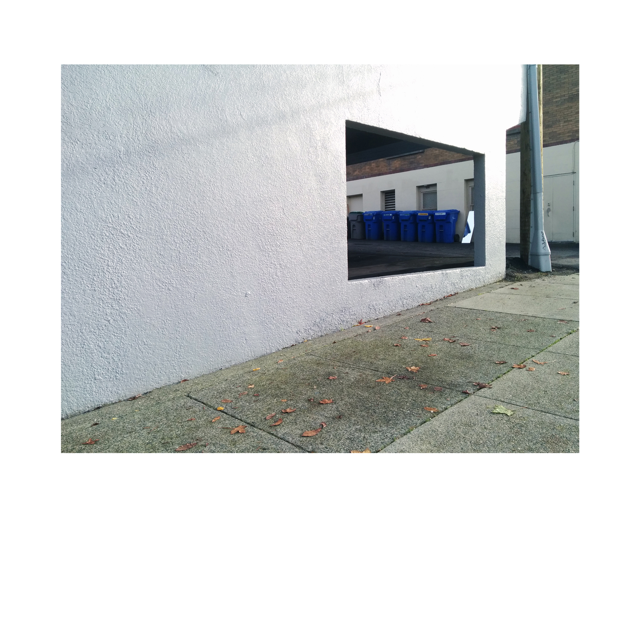 View of recycling bins through the cutout of a building garage in autumn