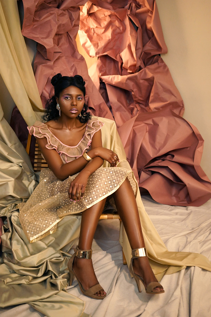 Model sits with arms and legs folded, surrounded by fabric