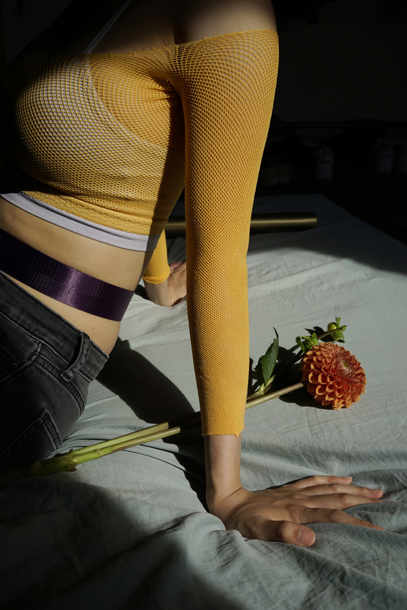 light falls lightly on the flower next to wei in an orange netted top with purple belt